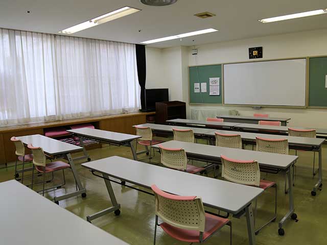 会議室です。正面にはホワイトボード、手前には長テーブルと椅子が並べられています。